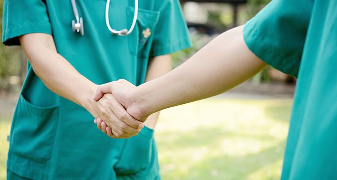 two carers wearing green scrubs shaking hands