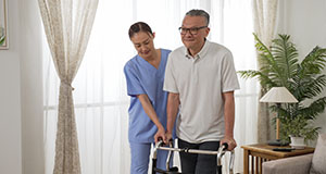 a nurse helping an elderly man with a walker around his house