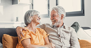 a happy elderly couple sitting on a sofa together smiling