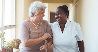 an elderly woman walking arm-in-arm down a hallway with a senior respite nurse