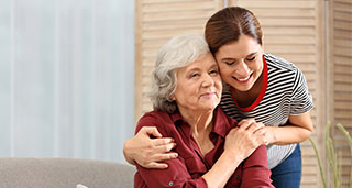 a woman in a striped shirt smiling and providing companionship next to an elderly lady