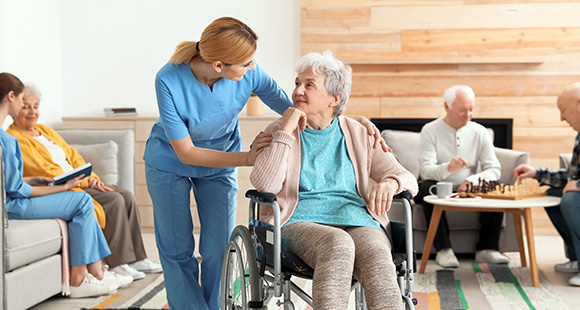 a nurse speaking with an elderly lady in a wheelchair in the living room of a care home