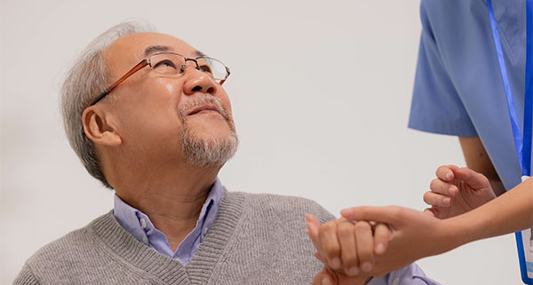 an elderly man holding the hand and looking up at a nurse