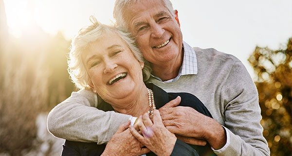 an elderly couple smiling and bracing with one behind the other 