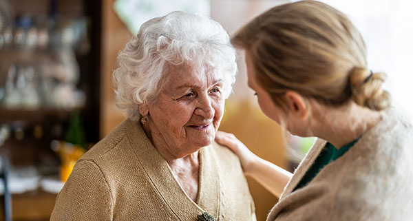 an older woman with dementia smiling at a carer opposite of her