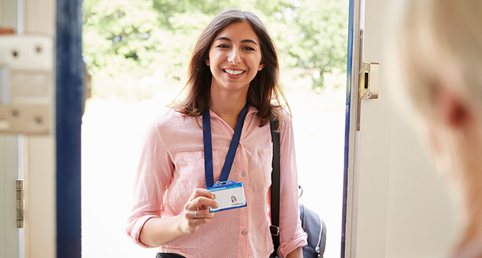 a female carer showing an ID badge as she enters the home of an elderly person